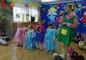 Nauczycielka w przebraniu, cztery dziewczynki przebrane za księżniczki przygotowują się do konkursu. Pozostałe dzieci siedzą.